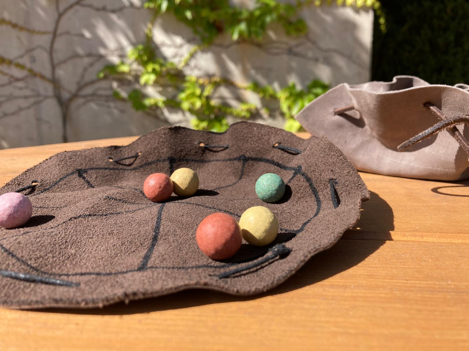 selbstgemachte Beutel aus Leder sowie bunte kleine Murmeln liegen auf einem Holztisch
