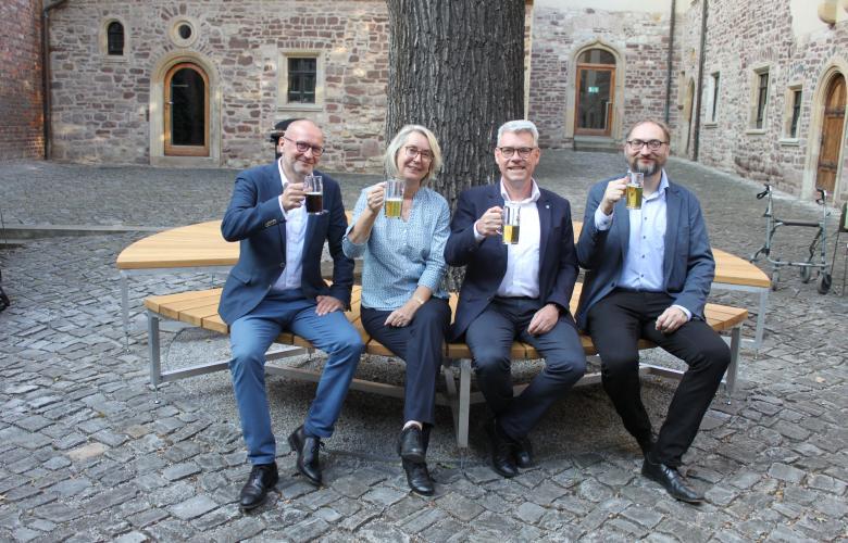4 Menschen sitzen auf Rundbank unter großem Baum, Steinboden