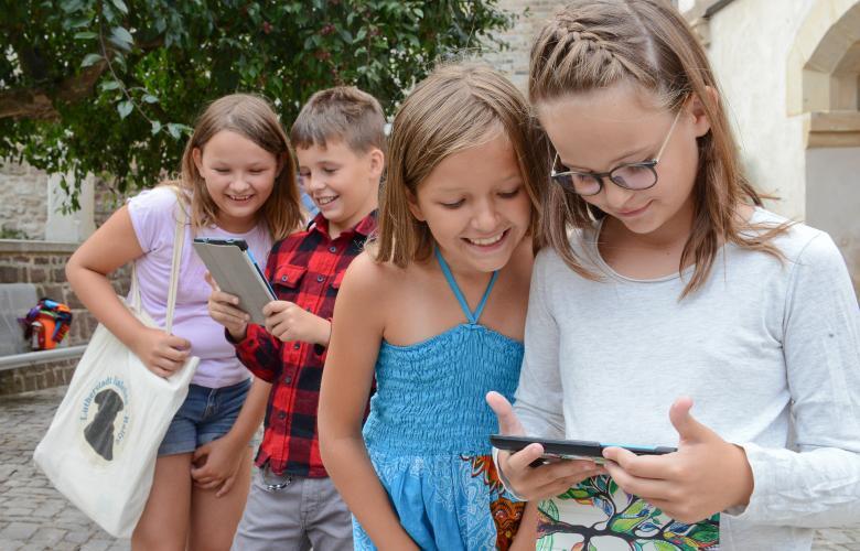 4 Kinder stehen in 2er Gruppen beisammen und schauen auf Tablets