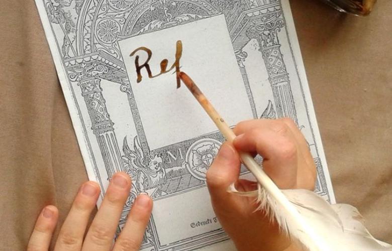 mit Feder schreibt eine Kinderhand "Reformation" auf ein Blattpapier 
