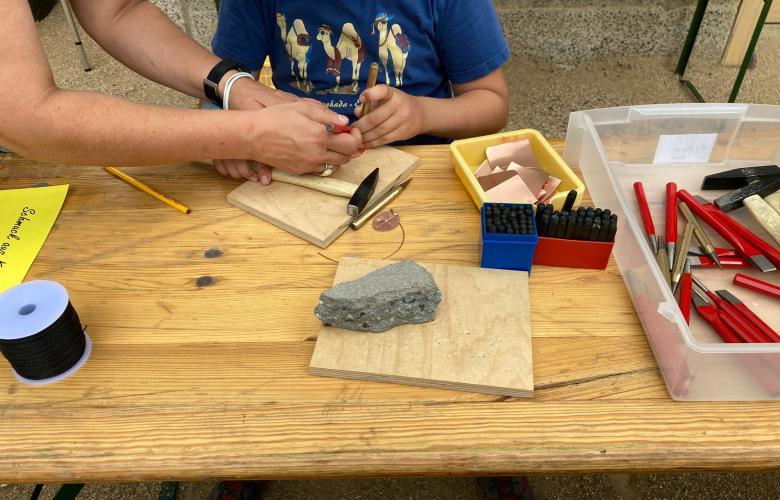 auf Tisch liegen verschiedene Materialien: Hämmer, Zangen, Holzbretter, Kupferplättchen