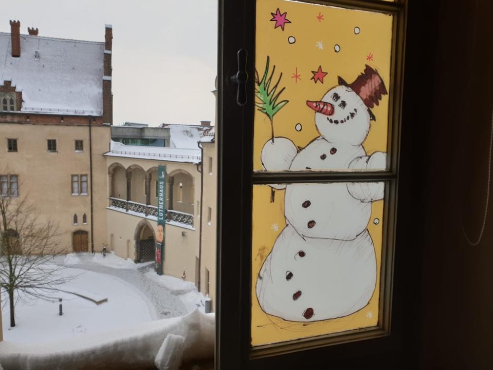 offenes Fenster, rechts Schneemannbild auf Fensterscheibe, links Blick auf verschneiten Hof des Lutherhauses