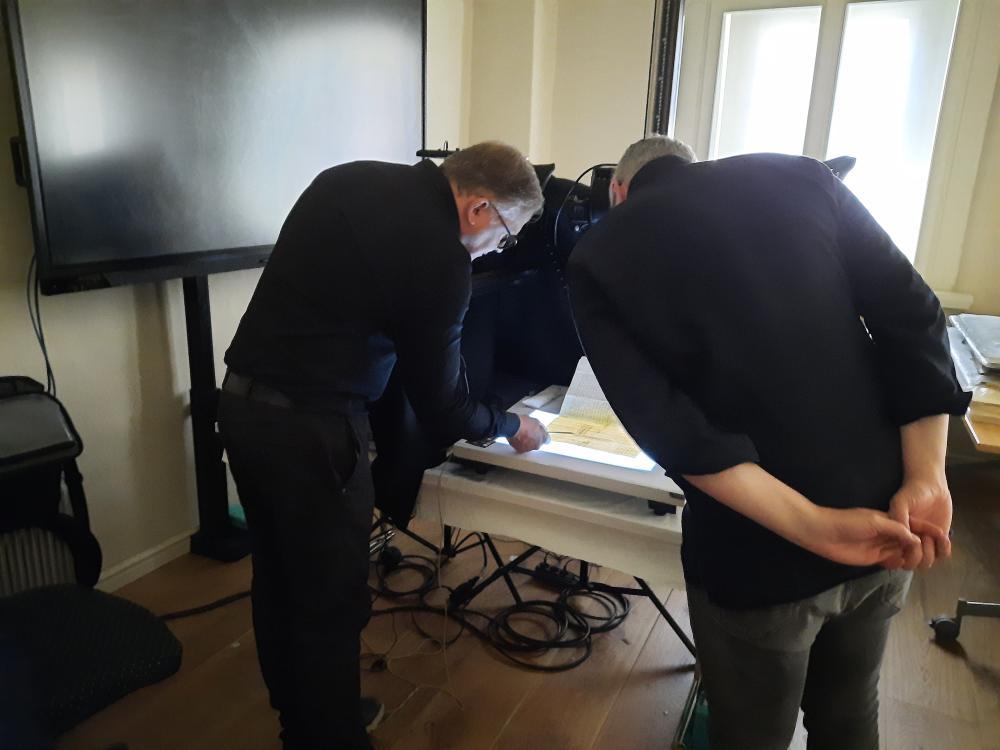2 Männer beugen sich über ein Schriftstück, dunkle Kleidung