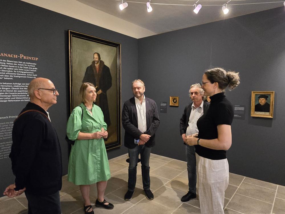 graue Wände, links großes Gemälde von Melanchthon, davor stehen 5 Menschen