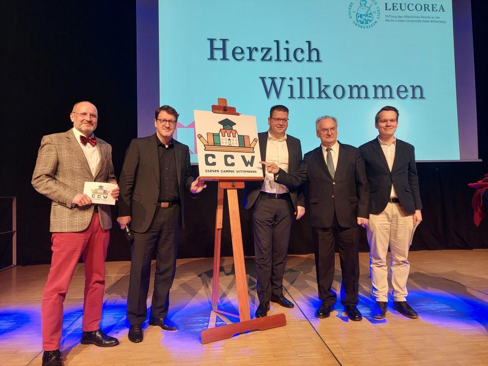 5 Männer aus Bühne, dahinter Leinwand