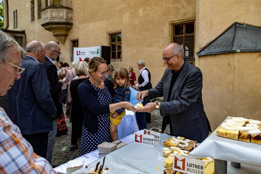 Bäcker steht am Kuchen, viele Menschen drumherum