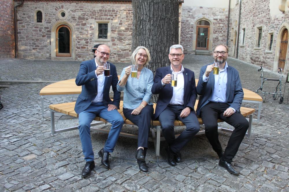 4 Menschen sitzen auf Rundbank unter großem Baum, Steinboden