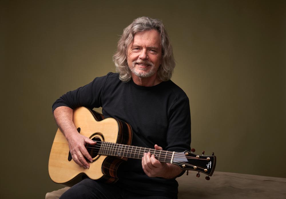 Paul Bartsch sitzend mit Gitarre in der Hand, schwarzer Pulli, längere Haare