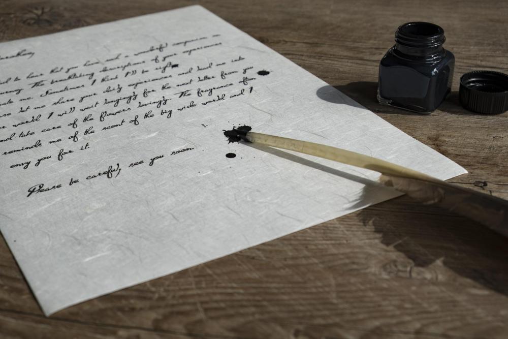 beschriebenes Papier, ein Tintenglas und eine Schreibfeder liegen auf Holztisch