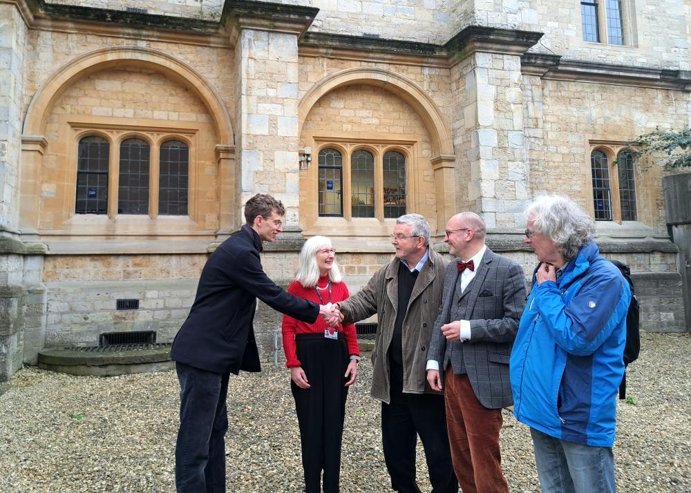 5 Menschen stehen im Halbkreis und begrüßen sich, Haus im Hintergrund