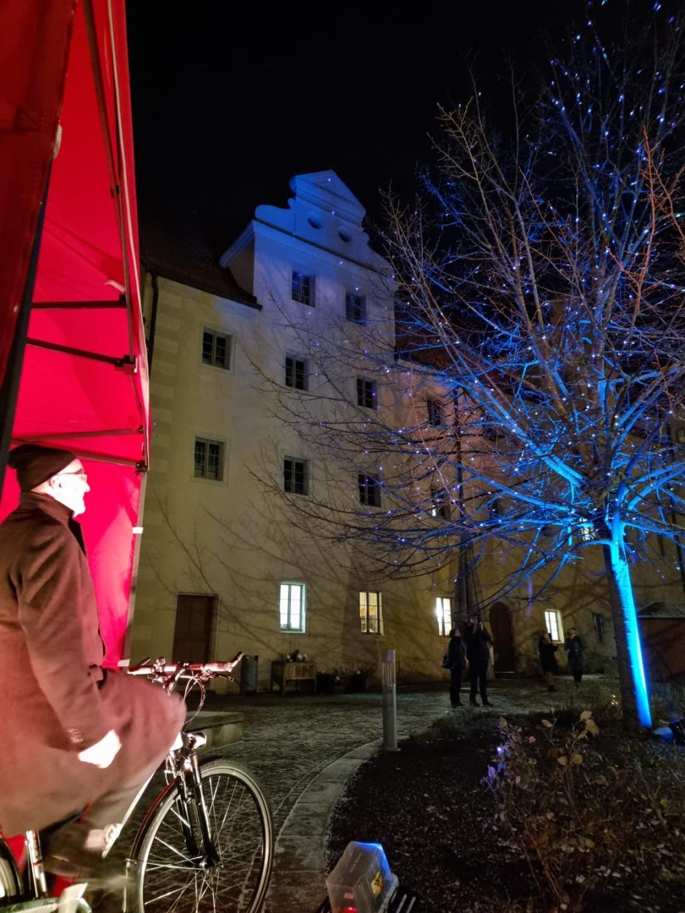 Stefan Rhein sitzt auf Fahrrad, Hintergrund Augusteum und angestrahlte Sommerlinde